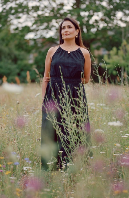 Nicci pictured standing in a field of wildflowers with her left arm bent behind her back holding the inner elbow of her right arm, wearing a long, sleeveless black dress