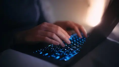 Getty Images Close-up hands of female using laptop in bed at night