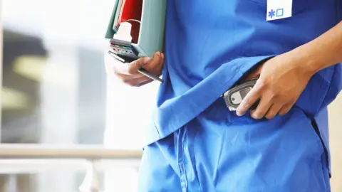 Getty Images A doctor dressed in blue scrubs puts a pager on his trousers.